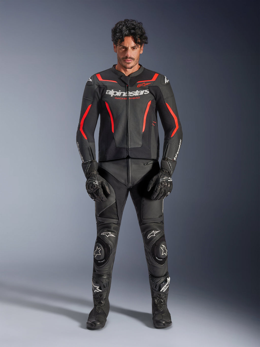 Mannequin homme portant la veste en cuir Alpinestars GP Force V2 Air en noir et rouge fluo, avec panneaux de poitrine perforés et logos blancs, associée à un pantalon de moto en cuir noir, des gants noirs et des bottes noires pour une tenue de course complète.