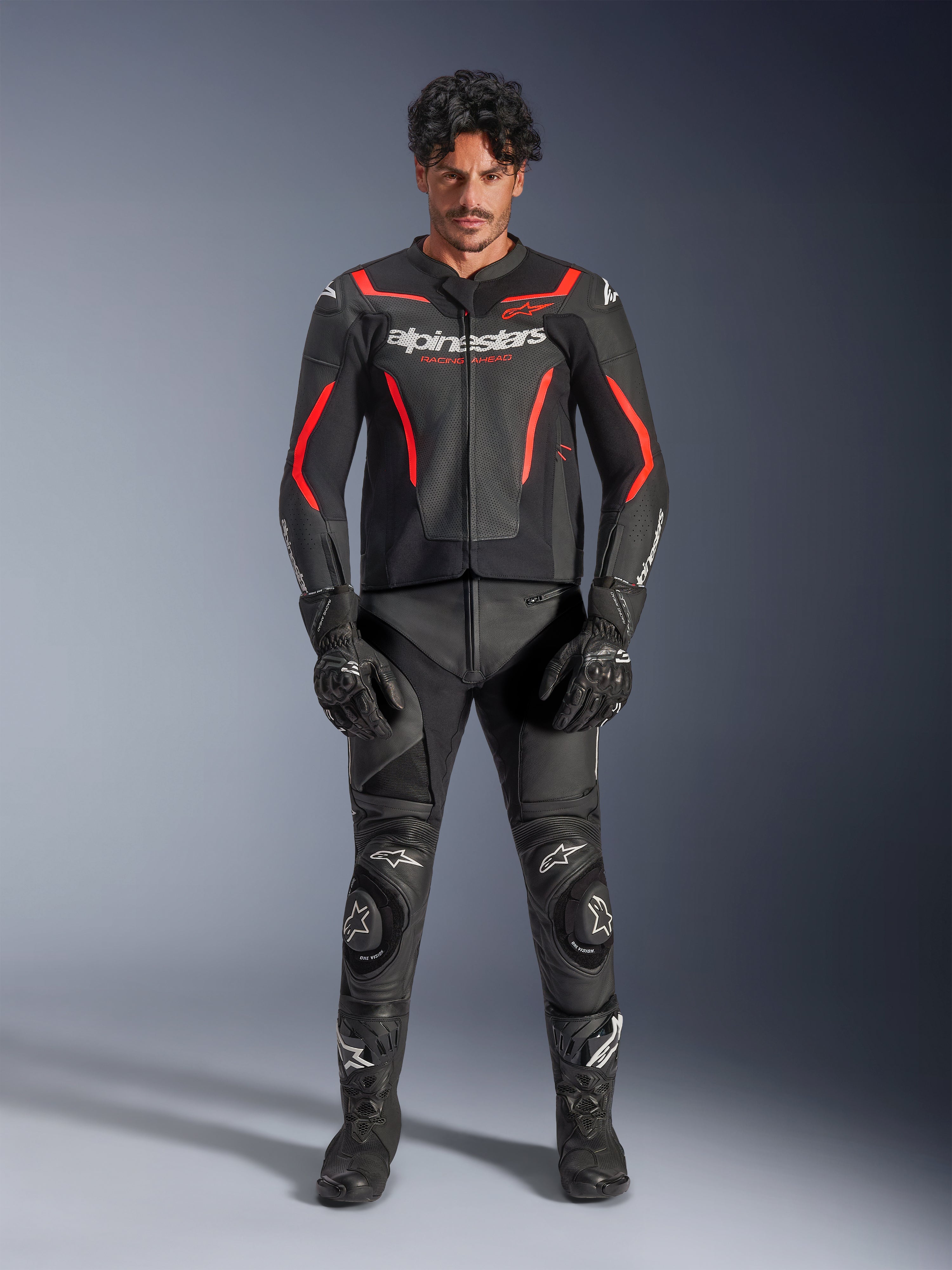 Mannequin homme portant la veste en cuir Alpinestars GP Force V2 Air en noir et rouge fluo, avec panneaux de poitrine perforés et logos blancs, associée à un pantalon de moto en cuir noir, des gants noirs et des bottes noires pour une tenue de course complète.