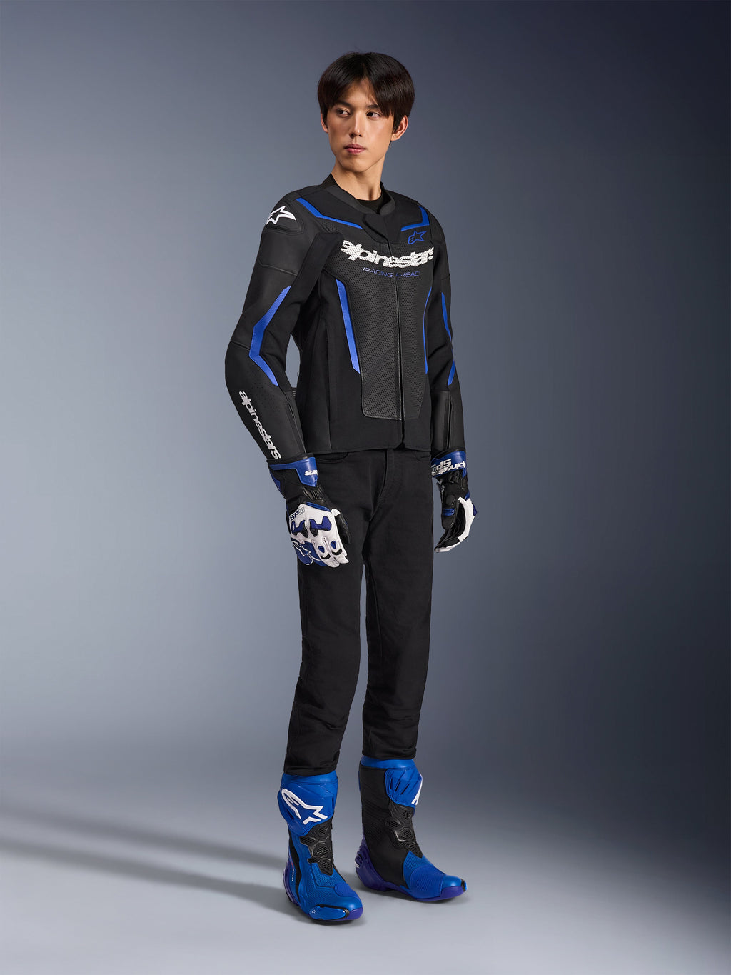 Pilote masculin portant le blouson en cuir GP Force V2 Airflow en Noir Bleu Métallisé, associé à des gants de course assortis et des bottes bleues, avec du cuir perforé et un marquage Alpinestars affirmé, équipement de route professionnel pour moto.