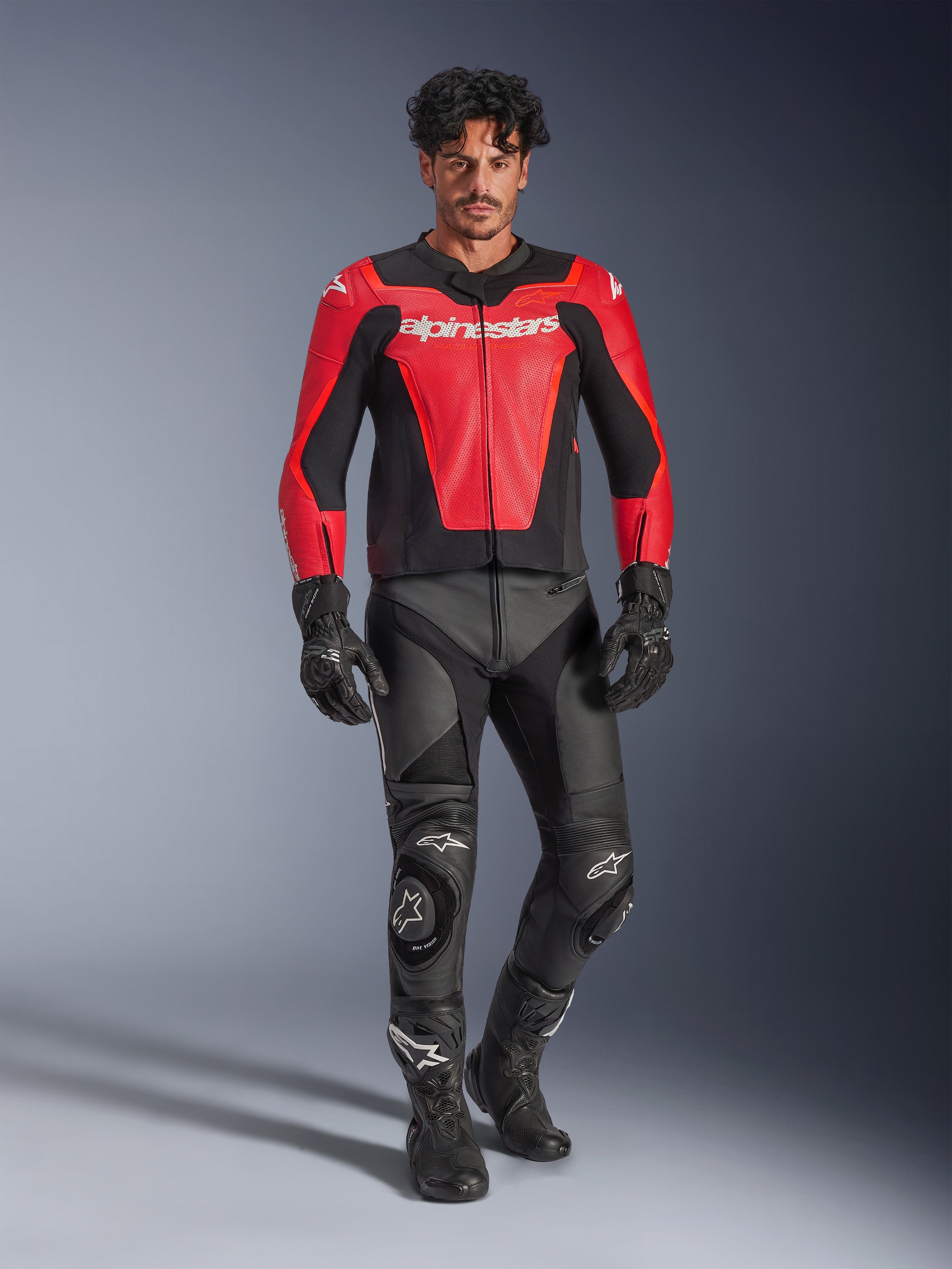 Alpinestars GP Force V2 Air Leather Jacket, Red and Black, perforated leather with white branding, worn by a model with black leather racing pants and gloves, professional motorcycle gear