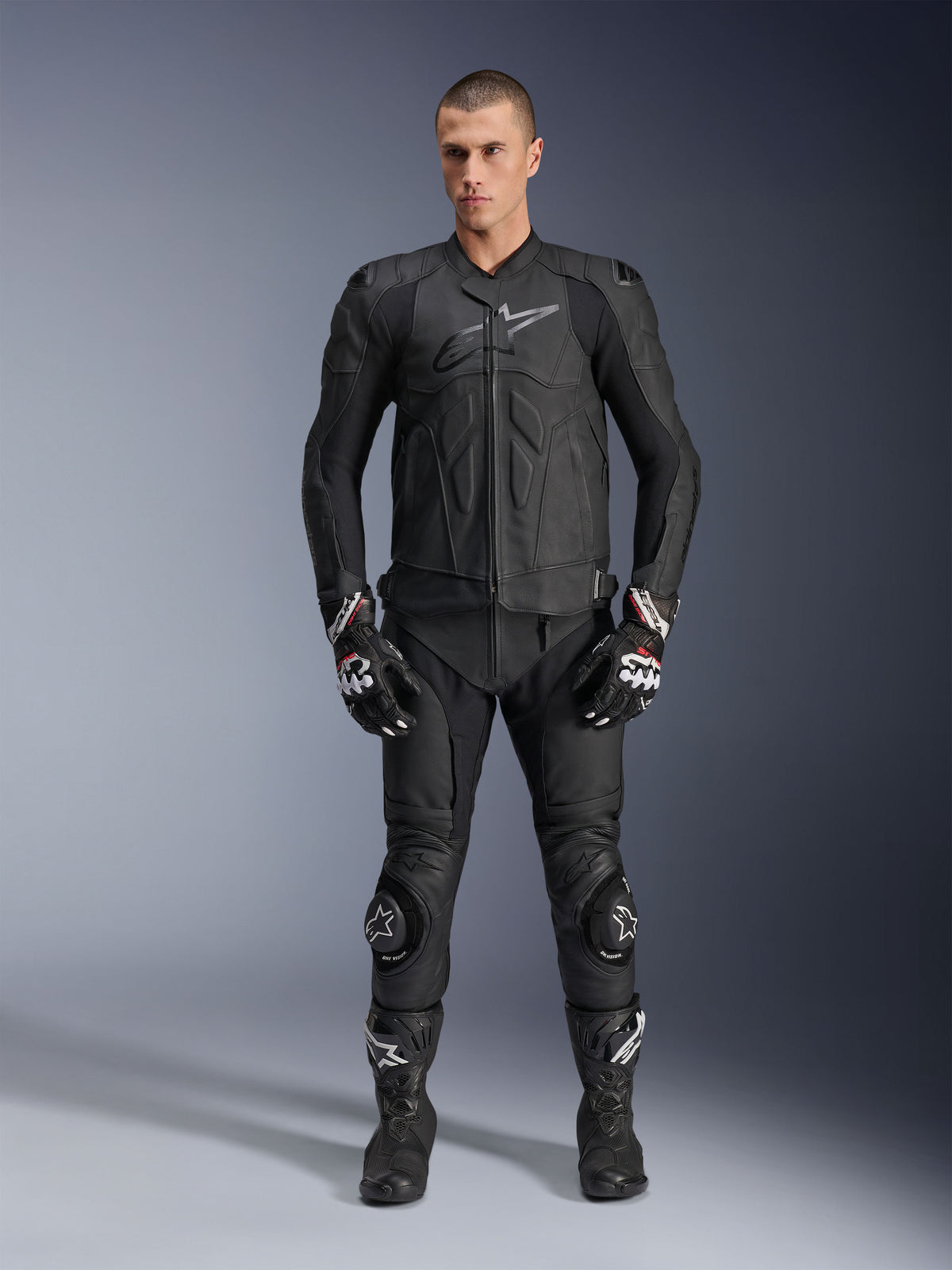 Alpinestars Dusk Leather Jacket, Black, worn by a male model as part of a complete racing-inspired outfit including matching leather pants, gloves, and boots, sleek ergonomic design with armored shoulders and chest branding.