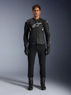 Veste en cuir Alpinestars Dusk Airflow, noir et blanc, veste de moto en cuir avec panneaux perforés pour la circulation de l'air, logo Astars blanc sur la poitrine, portée par un pilote avec pantalon noir, gants et bottes de moto, photo professionnelle en studio pour équipement de moto de sport.