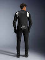 Veste en cuir Alpinestars Dusk Airflow, noir et blanc, vue arrière d'un pilote portant un pantalon et des bottes noirs, dotée de cuir perforé pour la ventilation, de panneaux stretch en accordéon blancs sur les épaules et d'un logo blanc sur le bas du dos