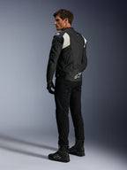 Veste en cuir Alpinestars Dusk Airflow, noir et blanc, vue arrière d'un mannequin portant la veste en cuir perforé avec pantalon et bottes noirs assortis, présentant des panneaux extensibles en accordéon blancs et un logo imposant dans le bas du dos, équipement de moto sport