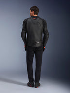 Veste en cuir Alpinestars GP Plus R V4 Airflow, noire, vue arrière du pilote portant l'équipement complet, cuir perforé pour la ventilation et logos rouges, design sportif ajusté, associée à un pantalon noir et des bottes de moto