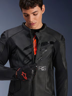 Veste en cuir Alpinestars GP Plus R V4 Airflow noire, modèle masculin entrouvrant la fermeture éclair pour montrer le logo interne orange, avec des panneaux en cuir perforé et un logo brillant sur la poitrine, accompagnée d'un gant de moto noir et rouge