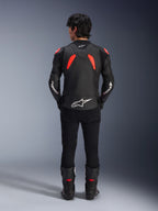 Veste en cuir Alpinestars GP Plus R V4 Airflow, Noir Rouge Fluo et Blanc, vue de dos sur un mannequin, avec des panneaux en cuir perforé et des logos blancs, portée avec un pantalon de moto noir et des bottes