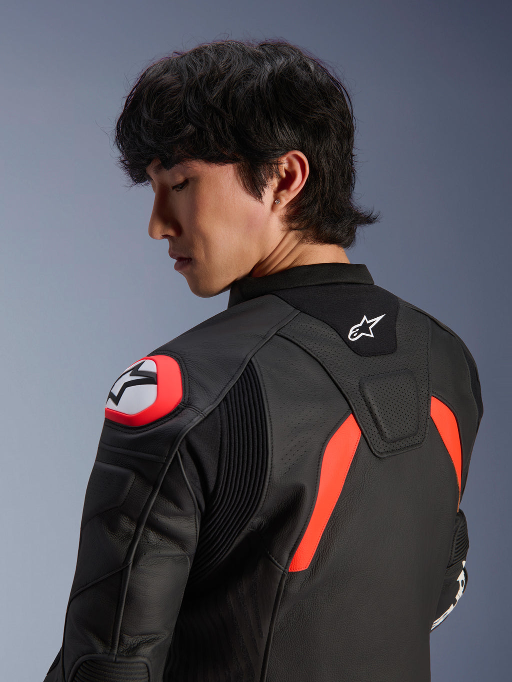 Veste en cuir Alpinestars GP Plus R V4 Airflow, noire avec accents rouge fluo et blanc, vue rapprochée du dos et de l'épaule sur un mannequin, avec zones en cuir perforé, logo Alpinestars et protections d'épaules intégrées pour la performance à moto.