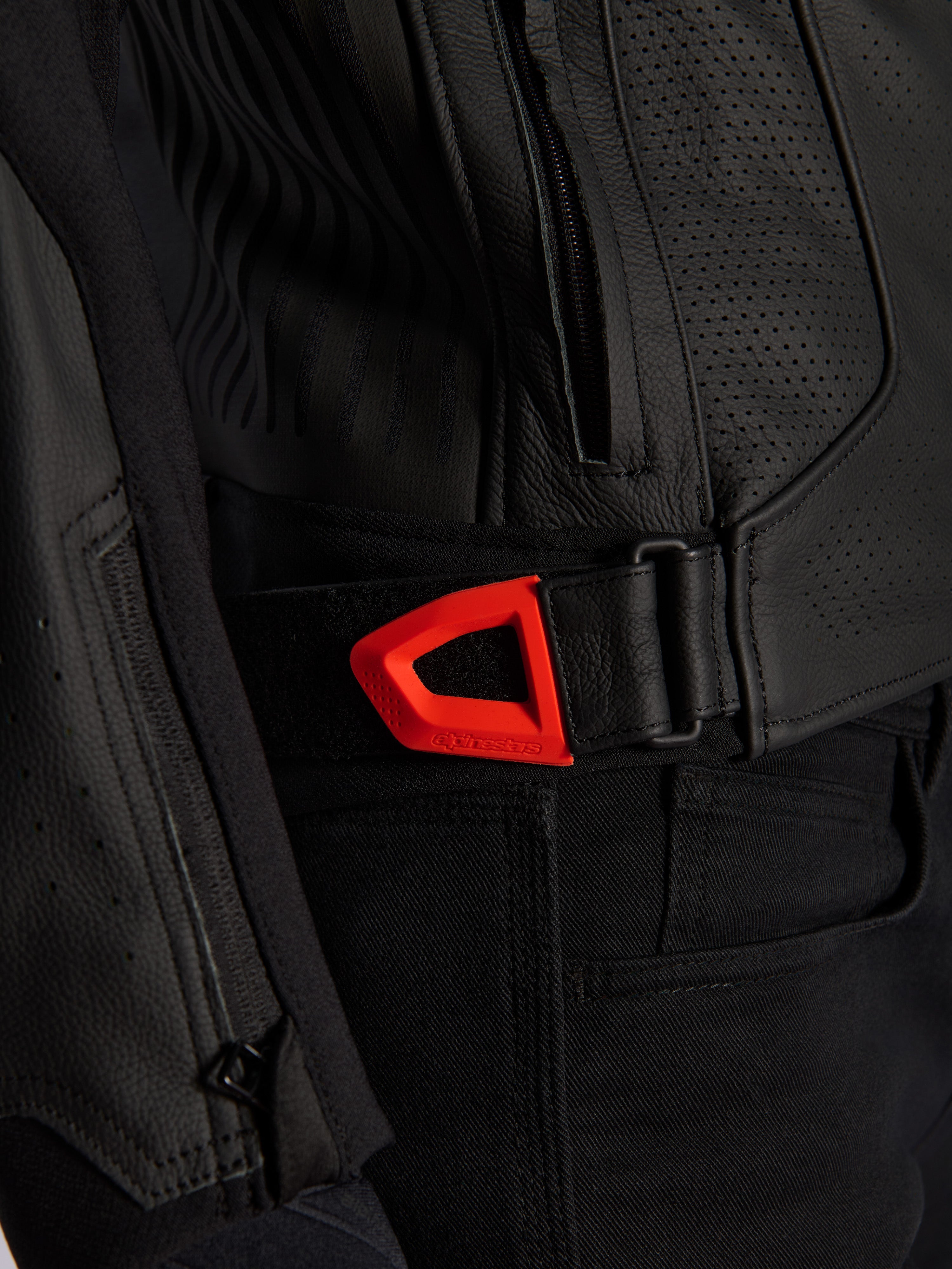 Veste en cuir Alpinestars GP Plus R V4 Airflow, gros plan, cuir perforé noir avec une sangle de réglage de la taille à crochet et boucle rouge fluo éclatant, dotée d'une poche latérale zippée et de panneaux texturés ergonomiques.