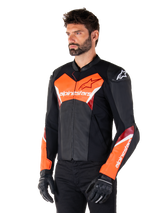 Veste en cuir Alpinestars Faster V3, noir et rouge fluo, veste de moto sportive haut de gamme avec des accents blancs et rouges, logo Alpinestars sur la poitrine et les manches, portée avec des gants et un pantalon de moto noirs.