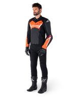 Male rider wearing the Alpinestars Faster V3 Leather Jacket in Black and Red Fluo, paired with black riding pants, gloves, and boots. The jacket features a race-derived silhouette with bold fluorescent red accents on the chest and sleeves, white Alpinestars branding, and a premium leather construction.