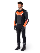Pilote portant la veste en cuir Alpinestars Faster V3 en noir et rouge fluo, associée à un pantalon, des gants et des bottes de moto noirs. La veste présente une silhouette inspirée de la course avec des accents rouge fluo vifs sur la poitrine et les manches, le logo Alpinestars blanc et une conception en cuir de qualité supérieure.