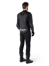 Veste en cuir Alpinestars Faster V3, veste de moto sportive, noir et rouge fluo, vue de dos portée avec un pantalon noir et des bottes noires, arborant l'inscription « alpinestars RACING AHEAD » sur le bas du dos et un petit logo d'étoile rouge, construction en cuir à coupe sportive épurée
