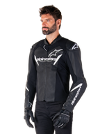 Veste en cuir Alpinestars Faster V3, veste de moto sport, noir et blanc, logo Alpinestars blanc proéminent et inscription « Racing Ahead » sur la poitrine, logos étoilés sur les épaules, construction en cuir premium avec panneaux extensibles, portée par un mannequin avec un pantalon et des gants noirs