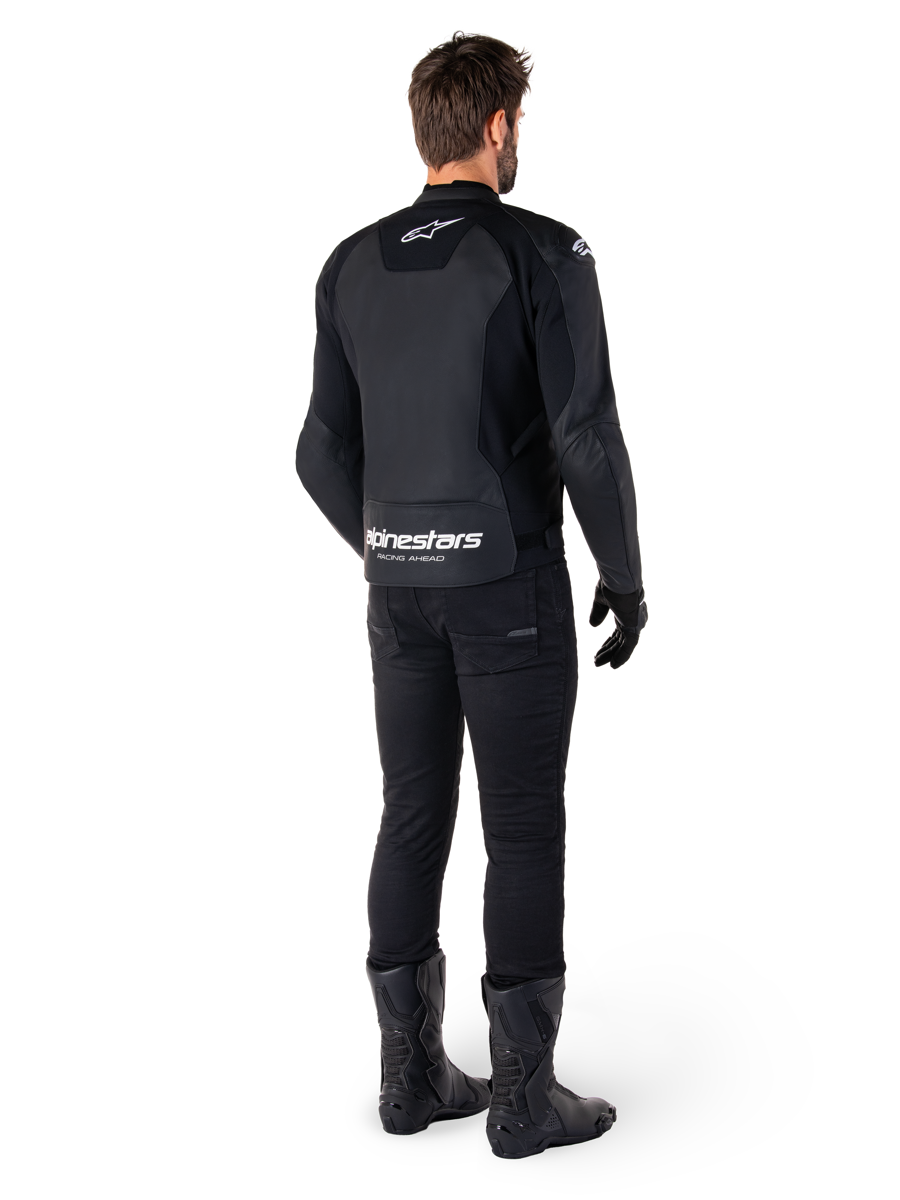 Veste en cuir Alpinestars Faster V3, vue de dos, noir et blanc, avec marquage 'alpinestars RACING AHEAD' sur le bas du dos, portée avec un pantalon et des bottes de moto noirs, veste de moto en cuir d'inspiration sportive avec panneaux extensibles