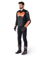Veste en cuir Alpinestars Faster V3 Airflow, noir et rouge fluo, portée par un mannequin homme avec un pantalon de moto noir, des gants et des bottes de course, dotée d'un cuir perforé et d'une silhouette sportive.
