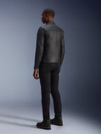Veste en cuir Alpinestars Blacktrack, noir, vue de dos montrant la coupe ajustée et les panneaux en cuir accordéon sur les omoplates, portée avec un pantalon noir et des bottes noires, veste de moto en cuir de bovin haut de gamme