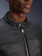 Gros plan de la veste en cuir Alpinestars Blacktrack, montrant la fermeture éclair métallique couleur canon de fusil et le bouton de fermeture au col avec logo Alpinestars, texture en cuir de bovin noir premium, vêtement de moto urbain