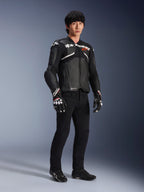 Veste en cuir Atem V5 Alpinestars, veste de course moto, noir et blanc, portée avec un pantalon noir et des gants assortis, avec le logo Alpinestars blanc sur la poitrine et des protections aux épaules.