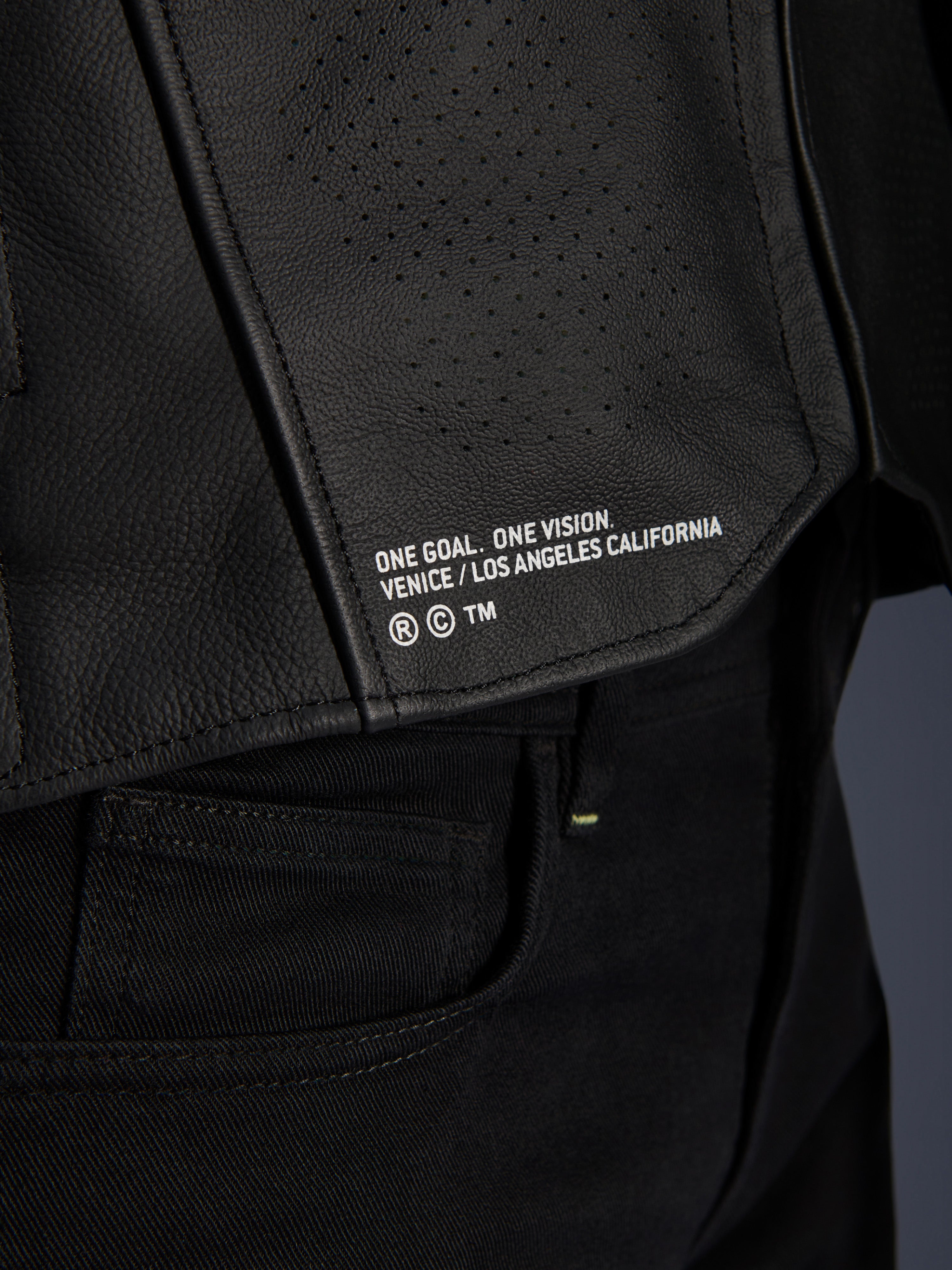 Gros plan sur la veste en cuir Alpinestars Atem V5 en noir, présentant le panneau inférieur du dos avec le marquage « ONE GOAL. ONE VISION. VENICE / LOS ANGELES CALIFORNIA » et une texture en cuir perforé.