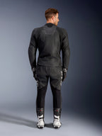 Vue de dos d'un homme portant le blouson en cuir Alpinestars Caliber noir, doté d'un logo embossé et de panneaux en cuir perforé, associé à un pantalon de moto en cuir noir, des gants noirs et des bottes de course blanches.