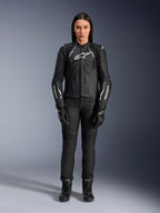 Veste en cuir pour femme Alpinestars Stella Dusk, noir et blanc, portée par un mannequin avec un pantalon et des bottes noirs assortis, vue de face, logos Alpinestars blancs sur la poitrine et les manches, équipement de protection en cuir bovin premium pour femme