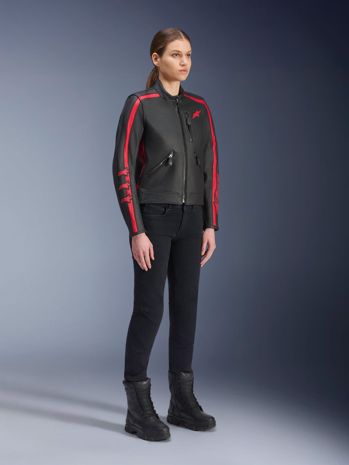 Mannequin femme portant la veste en cuir Alpinestars Stella Dyno en Noir Haute Rouge, avec pantalon et bottes noirs, veste de moto en cuir de style héritage avec bandes rouges sur les bras et logo rouge, équipement de route et urbain pour femme