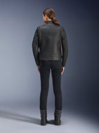 Vue arrière d'une femme portant la veste en cuir Alpinestars Stella Dyno, noir avec accents rouge Haute, associée à un pantalon noir ajusté et des bottes noires, design de veste de moto héritage moderne.