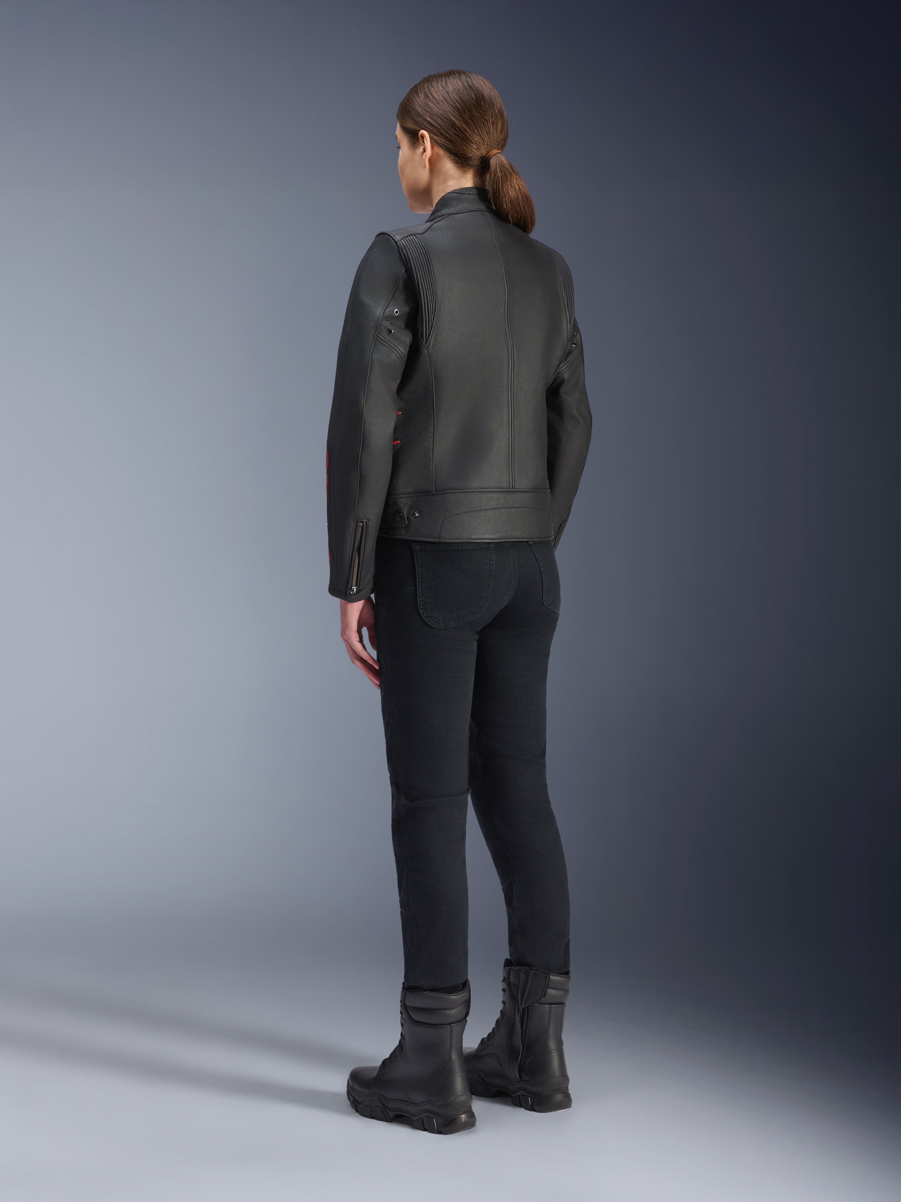 Veste en cuir Alpinestars Stella Dyno, veste de moto pour femme, Noir Haute Red, vue arrière, portée avec un pantalon de moto noir et des bottes noires, finition en cuir de première qualité au style héritage