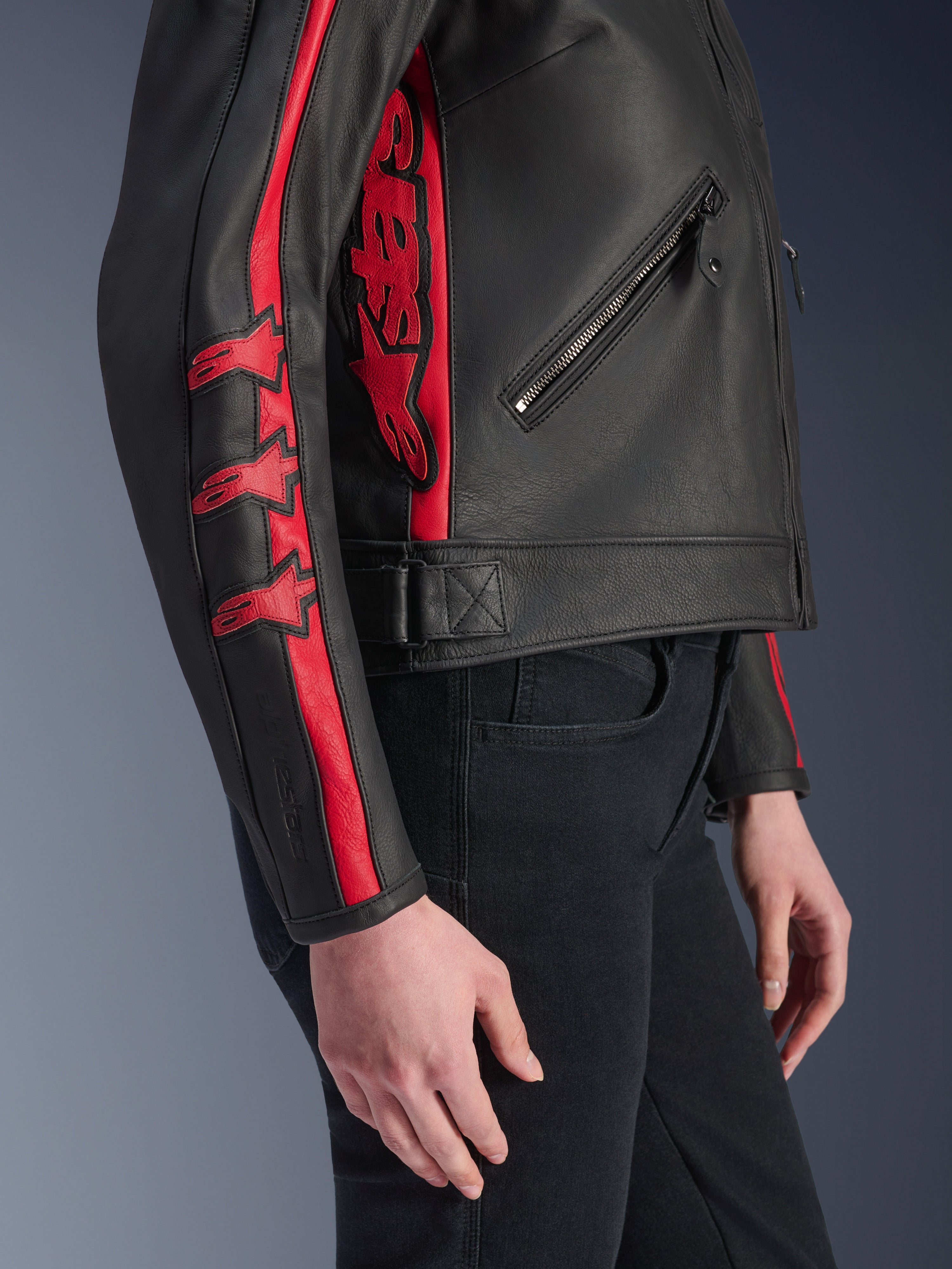 Veste en cuir Alpinestars Stella Dyno, veste de moto pour femme, noir et rouge haute, vue latérale portée par un mannequin, avec des bandes de course rouges et des logos en étoile sur la manche et un grand logo rouge sur le côté, cuir de bovin premium, style urbain