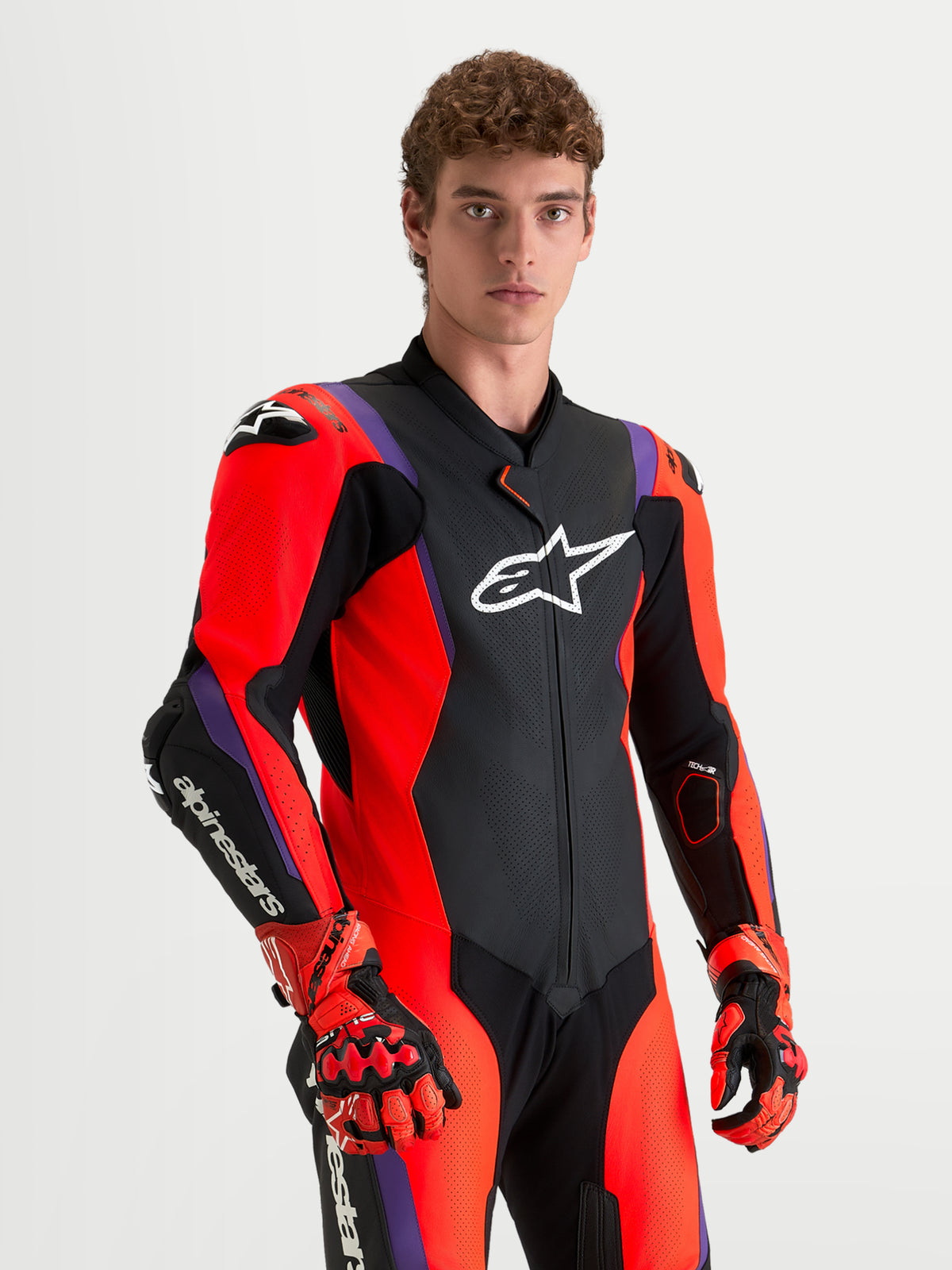 Combinaison en cuir Missile V3 1 Pc d'Alpinestars, combinaison moto pour homme noire, rouge et violette, avec protections d'épaules, portée par un modèle.