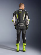 Combinaison en cuir Alpinestars GP Tech V5 1PC, vue de dos, noir, blanc et jaune fluo, avec bosse aérodynamique et logo étoile jaune, marquage Alpinestars blanc sur les manches et le dos, bottes de course jaune fluo assorties, équipement de moto professionnel pour circuit
