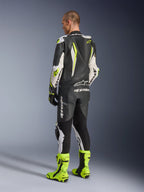 Combinaison en cuir Alpinestars GP Tech V5, noir, blanc et jaune fluo, vue arrière d'un pilote portant une combinaison de course complète avec bottes jaune fluo assorties, dotée d'une bosse aérodynamique et de logos Alpinestars, équipement de moto professionnel