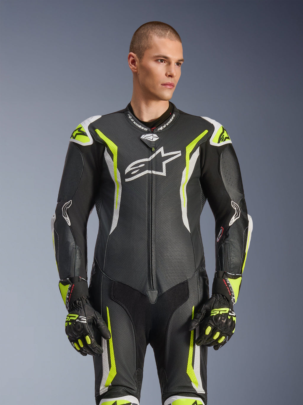 Combinaison en cuir Alpinestars GP Tech V5, noir, blanc et jaune fluo, équipement de course professionnel, cuir perforé avec grand logo Astar blanc sur la poitrine, accents jaune fluo et blancs, portée avec des gants de course assortis