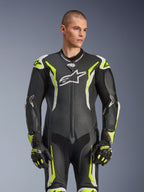 Combinaison en cuir Alpinestars GP Tech V5, noir, blanc et jaune fluo, équipement de course professionnel, cuir perforé avec grand logo Astar blanc sur la poitrine, accents jaune fluo et blancs, portée avec des gants de course assortis