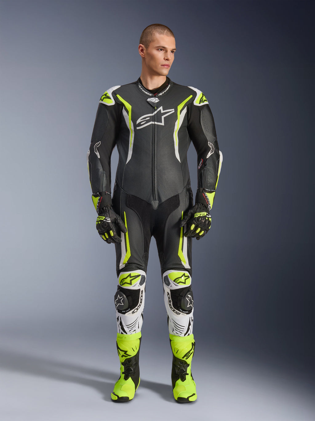 Alpinestars GP Tech V5 One Piece Leather Suit, combinaison de course moto professionnelle en noir et jaune fluo avec accents blancs, portée par un mannequin avec des gants et des bottes de course assortis, dotée d'un design aérodynamique et de sliders de protection.