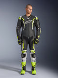 Alpinestars GP Tech V5 One Piece Leather Suit, combinaison de course moto professionnelle en noir et jaune fluo avec accents blancs, portée par un mannequin avec des gants et des bottes de course assortis, dotée d'un design aérodynamique et de sliders de protection.