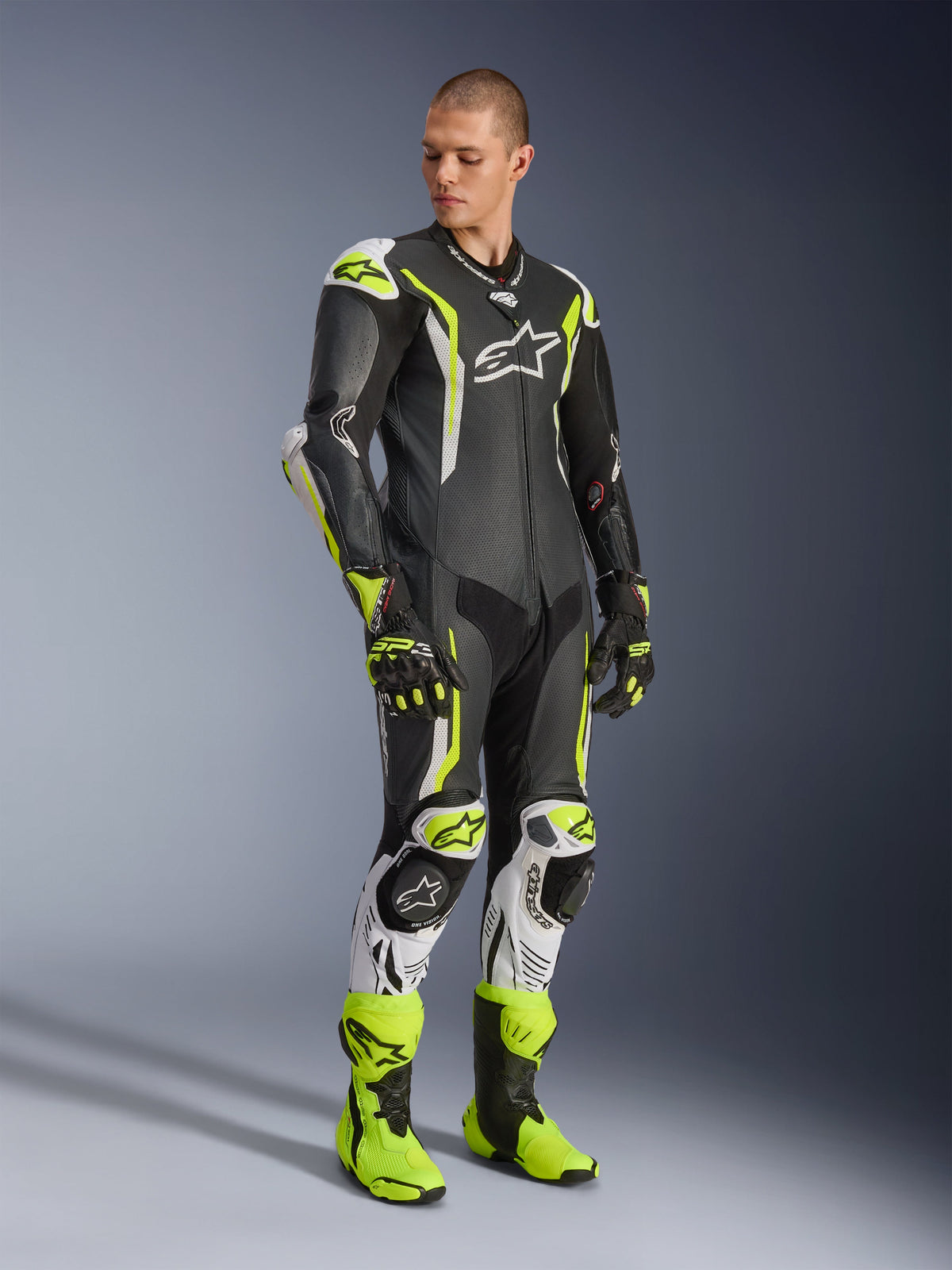 Combinaison en cuir une pièce Alpinestars GP Tech V5, noir, blanc et jaune fluo, portée par un mannequin avec des gants et des bottes de course assortis, équipement de course de moto professionnel offrant une performance aérodynamique et une protection contre les impacts.