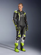 Combinaison en cuir une pièce Alpinestars GP Tech V5, noir, blanc et jaune fluo, portée par un mannequin avec des gants et des bottes de course assortis, équipement de course de moto professionnel offrant une performance aérodynamique et une protection contre les impacts.