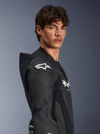 Mannequin homme portant la combinaison en cuir Alpinestars GP Force V2 1 pièce en noir, vue de profil mettant en valeur le logo étoile Alpinestars blanc sur la protection d'épaule DFS Lite, les panneaux en cuir perforé et la bosse aérodynamique.