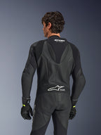Combinaison en cuir Alpinestars GP Force V2, une pièce, noire, vue de dos montrant le cuir perforé et les panneaux extensibles en accordéon, logos Alpinestars et Tech-Air Ready blancs sur le haut et le bas du dos, portée avec des gants noirs, équipement de course moto haute performance