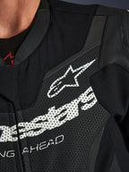 Combinaison de moto une pièce en cuir Alpinestars GP Force V2, gros plan sur la poitrine, cuir noir perforé avec grand logo Alpinestars blanc, équipement technique de conduite sportive, texture détaillée et branding