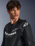Alpinestars GP Force V2 Leather Suit, gros plan d'un homme portant la combinaison noire, construction en cuir perforé, logo Alpinestars avec marquage « RACING AHEAD » sur la poitrine, logo étoile blanche sur les sliders d'épaules