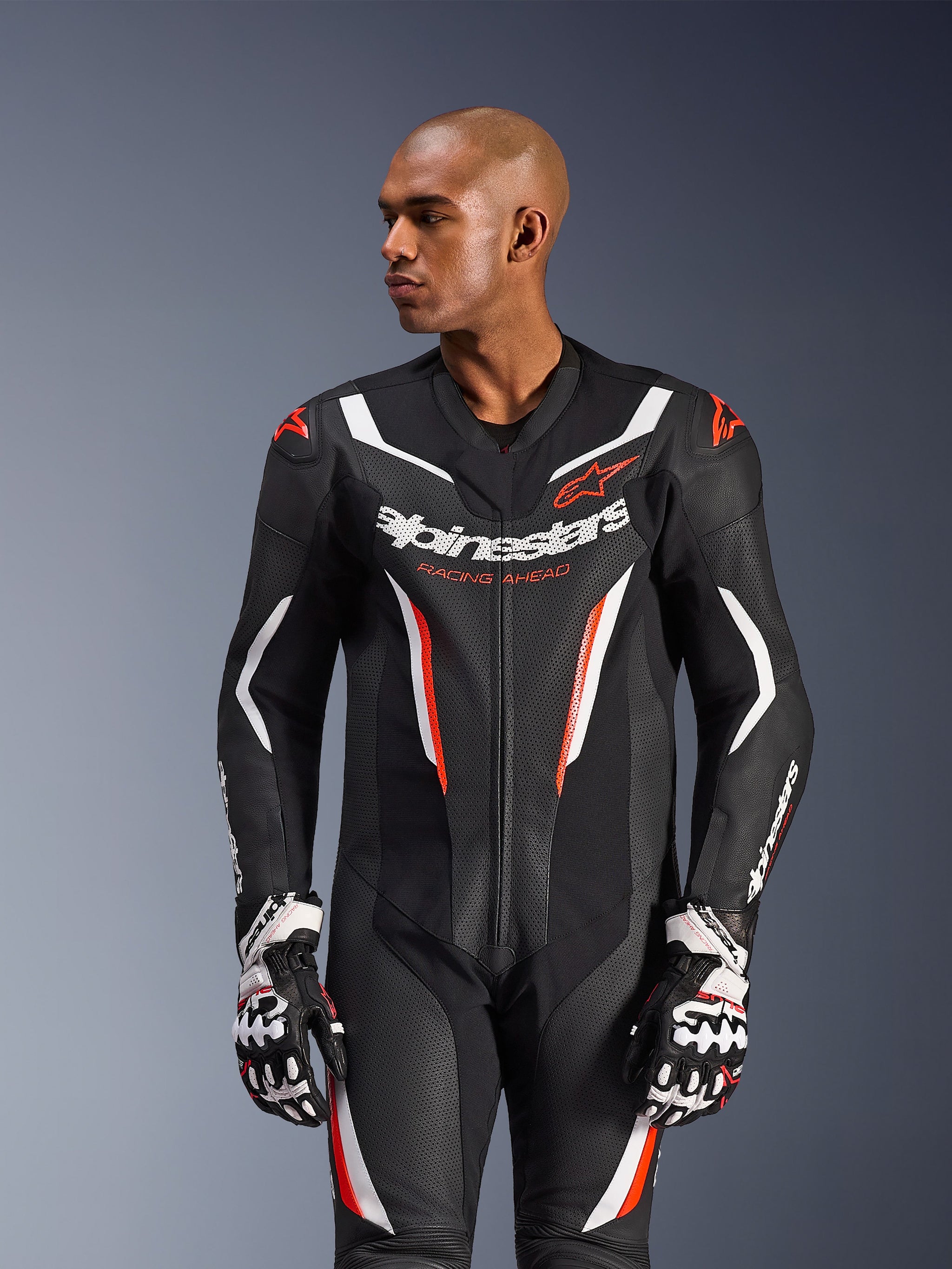 Combinaison en cuir Alpinestars GP Force V2 - 1 pièce, combinaison de course de moto, noir, blanc et rouge fluo, dotée de panneaux en cuir perforé, d'un logo imposant sur la poitrine avec l'inscription « Racing Ahead », et d'un design de protection ergonomique, portée avec des gants de course assortis