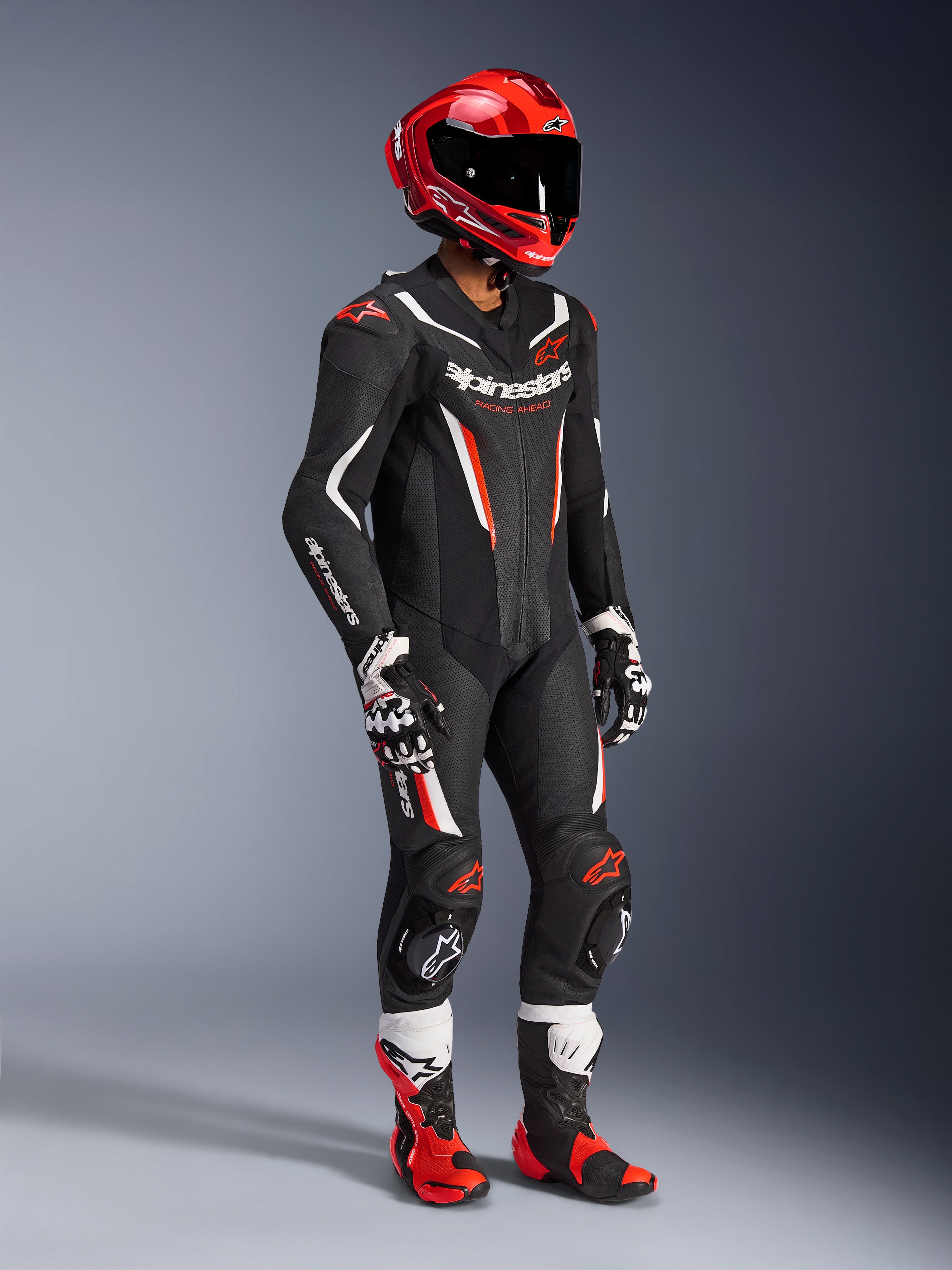 Combinaison en cuir Alpinestars GP Force V2 - 1 pièce, combinaison de course professionnelle noire, blanche et rouge fluo, avec panneaux en cuir perforé et protections DFS Lite, tenue de piste complète avec casque de course rouge, gants et bottes assortis.