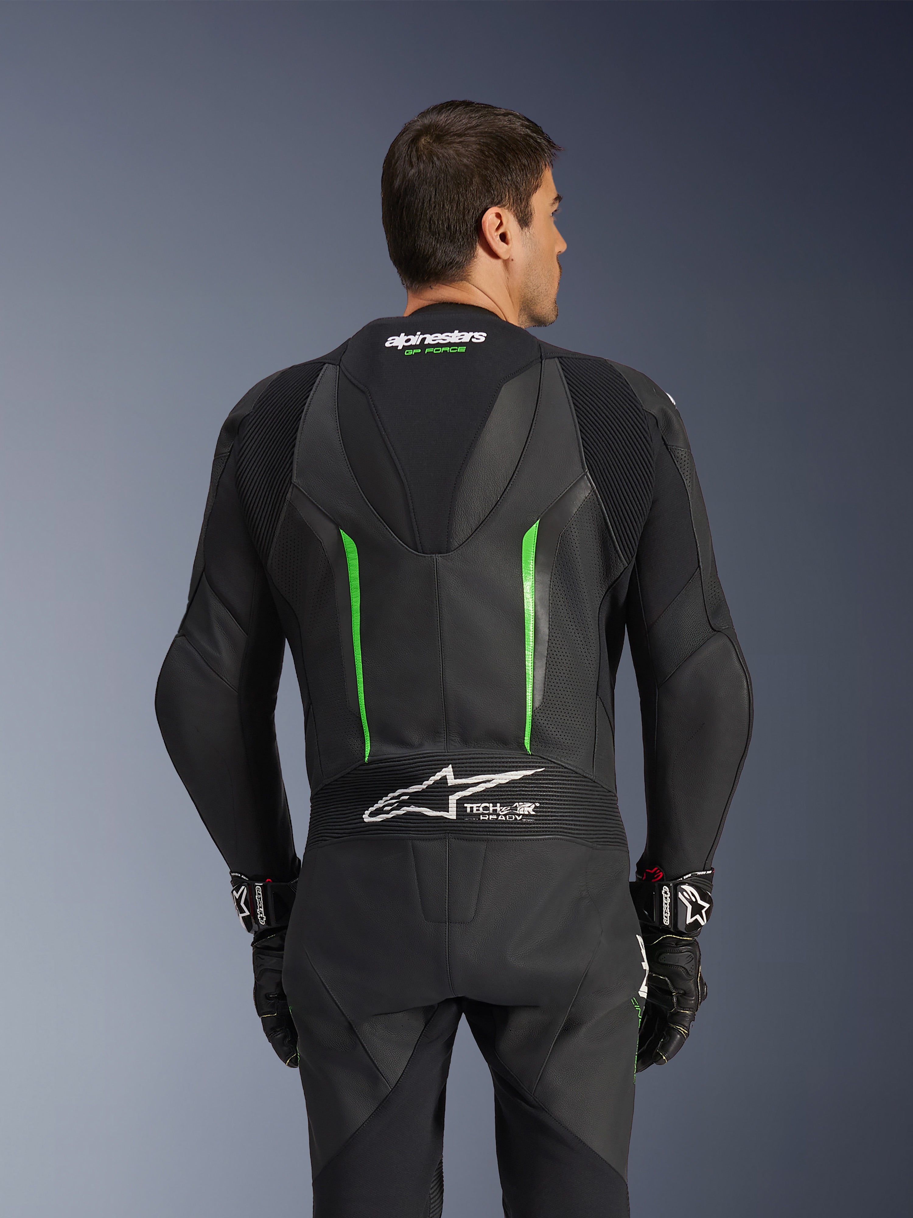 Alpinestars GP Force V2 Leather Suit - 1 pièce, noir et vert, vue arrière présentant la bosse aérodynamique, le marquage Tech-Air Ready, les zones en cuir perforé et les panneaux extensibles en accordéon pour la course moto