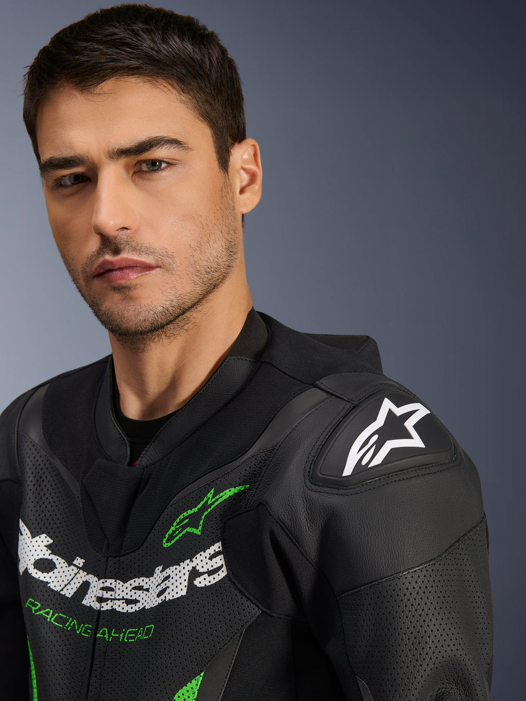 Alpinestars GP Force V2 Leather Suit - 1 pièce, noir et vert, gros plan d'un mannequin portant la combinaison de course moto, avec logos blancs et verts, panneaux en cuir perforé et protection d'épaule DFS Lite avec un logo étoile blanc.