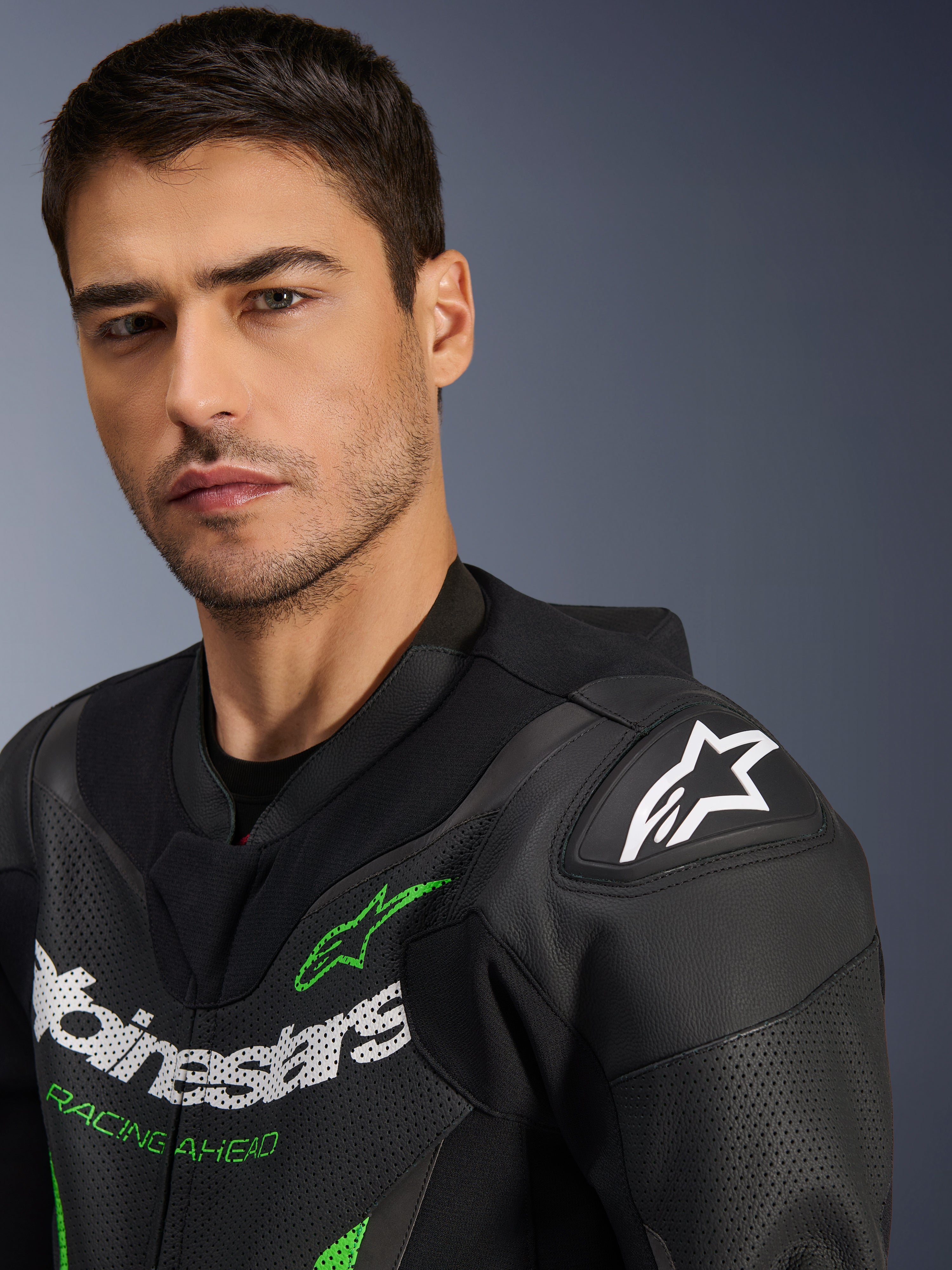 Alpinestars GP Force V2 Leather Suit - 1 pièce, noir et vert, gros plan d'un mannequin portant la combinaison de course moto, avec logos blancs et verts, panneaux en cuir perforé et protection d'épaule DFS Lite avec un logo étoile blanc.