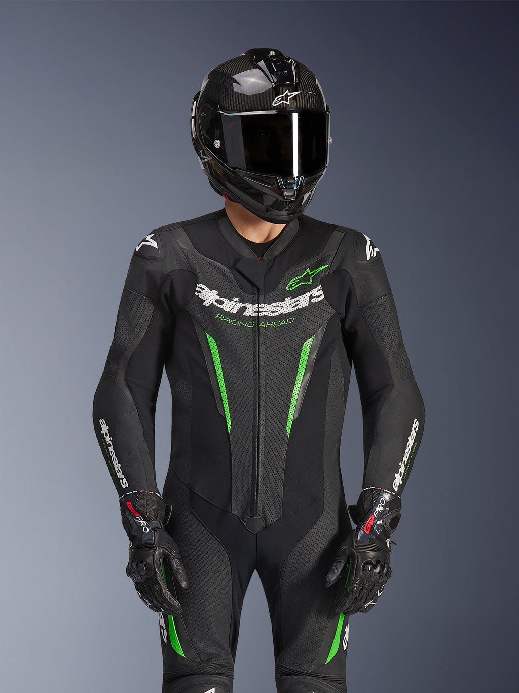 Combinaison en cuir Alpinestars GP Force V2 1 pièce, noir et vert, combinaison de course de moto portée avec un casque en fibre de carbone et des gants GP Pro, avec des accents vert lime et le marquage Alpinestars « Racing Ahead », conçue pour la performance sur piste