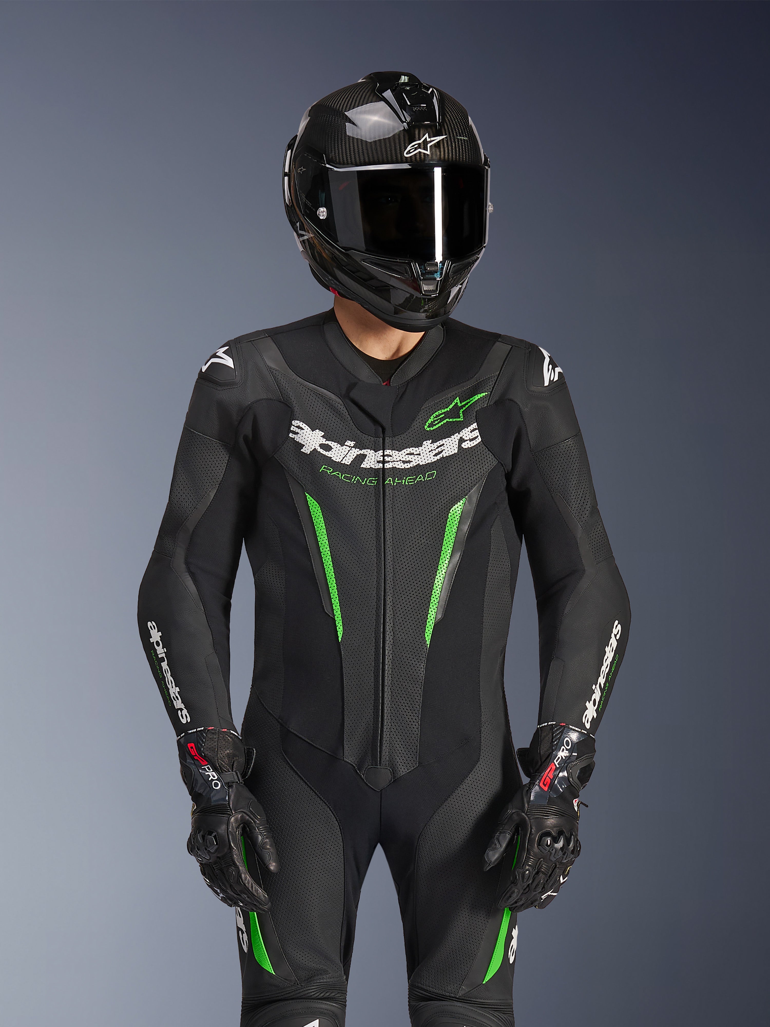 Combinaison en cuir Alpinestars GP Force V2 1 pièce, noir et vert, combinaison de course de moto portée avec un casque en fibre de carbone et des gants GP Pro, avec des accents vert lime et le marquage Alpinestars « Racing Ahead », conçue pour la performance sur piste